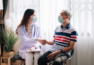 Asian doctor visit and examines a senior man at home ,shaking hands after finished health check up ,hospital services ,and wearing a mask to protect covid-19.