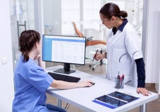 Stomatolog and nurse in tooth clinic checking patient appointment looking at computer monitor. Stomatology assistant and teeth doctor discussing in reception of dental office